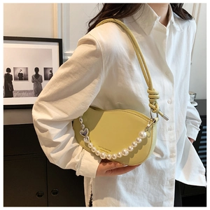Detail of light yellow half-moon bag featuring pearl chain and silver heart pendant