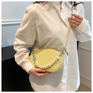 Detail of light yellow crescent bag with decorative pearl chain and silver heart charm