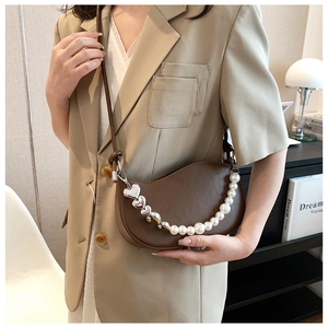 Detailed view of dark brown crescent bag with heart and pearl chain on a beige blazer