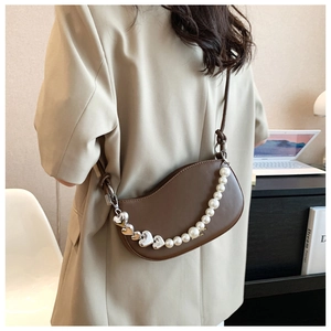 Close-up of brown crescent handbag with pearl and heart chain in an office setting