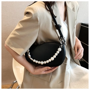 Detail of a black leather crescent underarm bag with decorative pearl chain on beige blazer