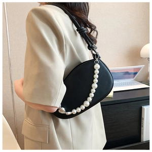 Detail of a black matte leather bag featuring an elegant white pearl chain and knotted strap