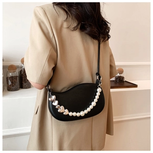 Close-up of black crescent shoulder bag with pearl and silver heart chain on beige blazer