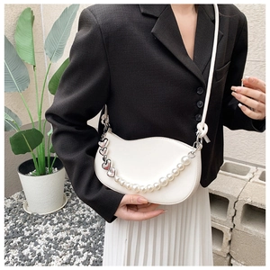 Close-up of white semi-circular leather bag with luxury pearl and heart chain detail