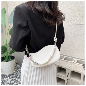 Close-up of a white half-moon bag featuring elegant pearl and heart metal chains