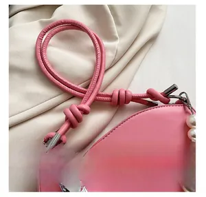 Detail of pink shoulder bag featuring pearl chain, heart charm, and knotted strap accents