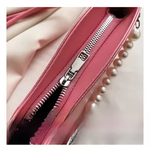 Detail of pink leather bag featuring smooth silver zipper and elegant pearl chain handle