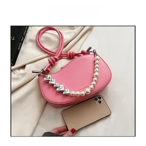 Detailed view of pink semi-circle bag with decorative pearl and heart chain strap