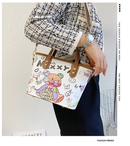 Detail der weißen Leder-Beuteltasche mit bunten Cartoon-Graffiti und braunen Griffen