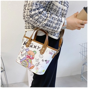 Detail einer trendigen Graffiti-Handtasche mit braunen Ledergriffen zu einem Karomantel