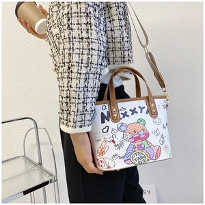 Detail der weißen Graffiti-Beuteltasche mit buntem Bärenprint und braunen Ledergriffen