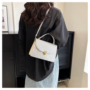 Detail of silver glitter crossbody bag featuring a gold twist lock and beige leather handle