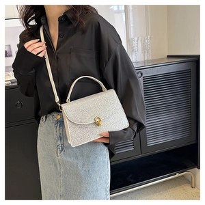 Detail of silver sequin crossbody bag with gold twist lock worn on a shoulder