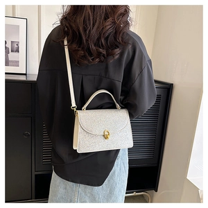 Detailed view of a silver glitter crossbody bag with a golden round twist lock on a model