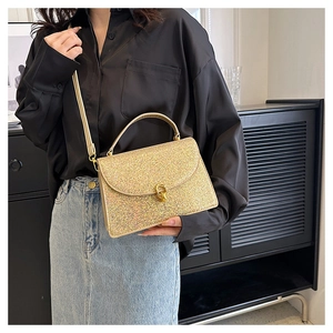 Detail of gold sequin crossbody bag with metal lock and handle on black outfit