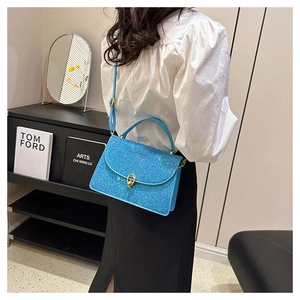 Close-up of sparkling blue sequin crossbody bag with gold metal clasp on a female model