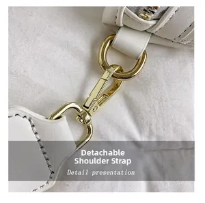 Detail des abnehmbaren breiten Schultergurts mit goldener Metallschnalle an weißer Tasche