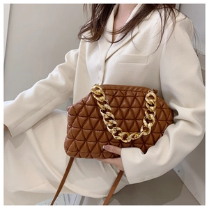 Brown quilted handbag with a chunky gold chain strap worn over a white suit jacket