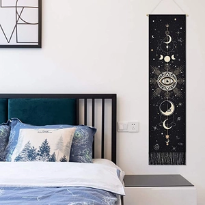 Bohemian moon phase and eye tapestry with black fringe on a light bedroom wall