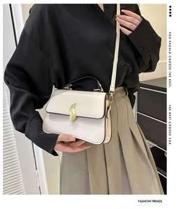 Détail du sac bandoulière beige minimaliste avec poignées noires et fermoir feuille dorée