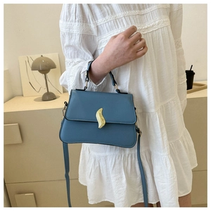 Sac à main en cuir bleu porté par un mannequin avec boucle dorée et robe en dentelle