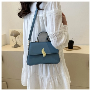 Détail du sac bandoulière bleu Morandi avec boucle dorée en S dans une pièce minimaliste