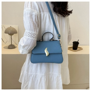 Détail du sac bandoulière bleu clair avec fermoir doré sur une robe en dentelle