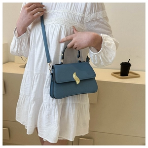 Détail d'un sac bandoulière bleu clair avec un fermoir en métal doré de forme ondulée