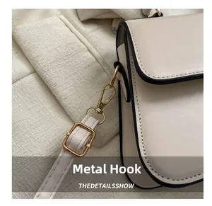 Détail du crochet en métal doré et bordure noire sur un sac à main en cuir crème