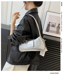 Détail du sac sous le bras argenté avec effet crocodile, logo doré et fermoir aimanté