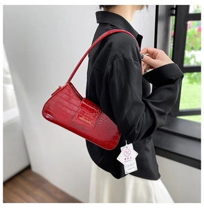 Détail du sac baguette rouge à motif crocodile avec surface polie et logo métallique