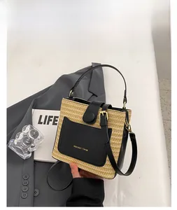 Détail du sac seau en paille tressée avec poche en cuir noir et logo doré brillant