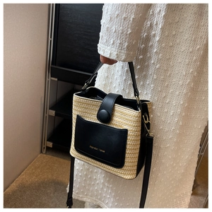 Détail du sac seau en paille tressée avec accents en cuir noir et logo doré imprimé