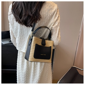 Détail d'un sac seau en paille tressée avec finitions en cuir noir porté par un mannequin