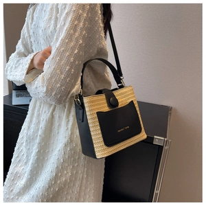 Détail du sac seau en paille tressée avec lanières en cuir noir et logo doré