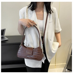 Gros plan détaillé du sac à bandoulière marron motif crocodile avec logo doré et boucle aimantée