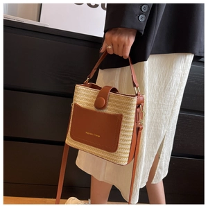 Détail du sac seau en paille tressée avec garniture en cuir marron et boucles en métal