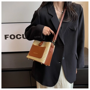 Femme en blazer noir portant un grand sac seau tissé avec détails en cuir marron