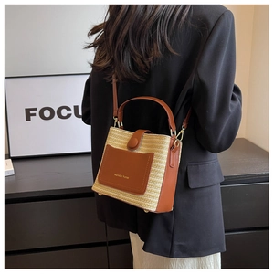 Détail du sac seau en paille tressée avec poche en cuir marron et bandoulière