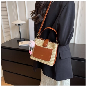 Détail d'un sac à bandoulière en paille tressée avec poche en cuir et charm rose