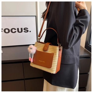 Détail d'un sac seau tissé avec garniture en cuir marron et accessoire pompon rose