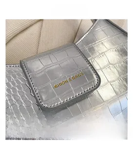 Gros plan détaillé du cuir argenté gaufré crocodile avec lettrage de marque doré sur le sac