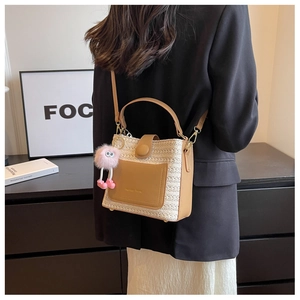 Détail d'un sac seau en paille tressée avec bordure en cuir marron et breloque rose