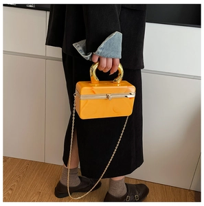 Model carrying a yellow acrylic box clutch with a gold U-shaped handle and chain strap