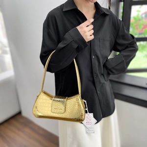 Sac baguette doré métallisé effet crocodile porté par un mannequin dans un décor minimaliste