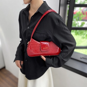 Sac baguette rouge à motif crocodile et lettrage doré porté sur une chemise noire