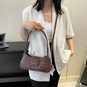 Sac baguette marron à motif crocodile porté à l'épaule par un mannequin en blazer blanc