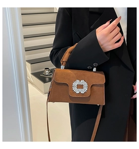 Detail of a brown suede handbag with a luxury crystal buckle shown on a model