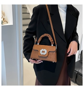Detail of brown suede handbag with crystal buckle and ruched handle on a black blazer
