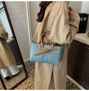 Close-up of light blue denim crossbody bag with brown leather straps on a trench coat model